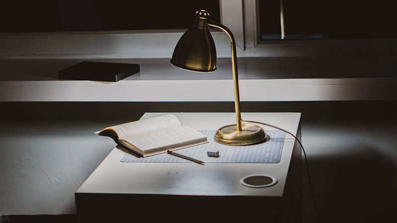 Lámpara de escritorio dorada iluminando un libro abierto en un espacio de estudio